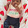 baby, infant, child, portrait, lying_down, pink_bow, headband, bib, text_on_clothing, strawberry_blanket, blanket, clothing, pants, socks, hand, fingers, face, indoors, carpet, cute