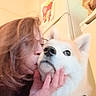 Saïka participe au concours pour gagner de l'argent avec cette photo : person, dog, indoor, kiss, affection, glasses, purple_sweater, white_dog, fluffy, harness, kitchen, refrigerator, utensils, hand, face, pet, love, cozy, close_up, expression