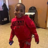 child, boy, smiling, indoors, red_clothing, hoodie, pants, sneakers, basketball, card, floor, door, high_chair, wall, person, casual, portrait, happy, playful, home
