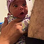 baby, child, headband, purple, floral_clothing, hand, adult_hand, indoor, door, surprised_expression, person, face, skin, closeup, portrait, infant, cute, newborn, holding, human