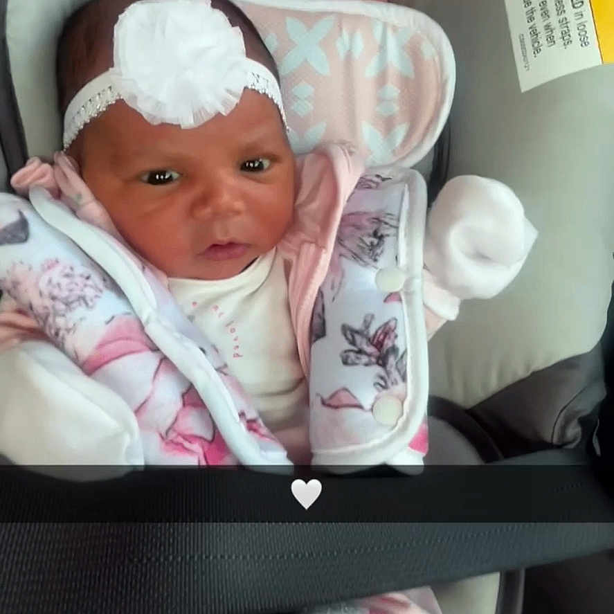 Namylah is registered to the contest to win money with this photo: baby, car_seat, child, closeup, clothing, cushion, cute, headband, indoor, infant, jacket, mittens, newborn, person, pink, portrait, safety_belt, seat, warning_label, white_flower