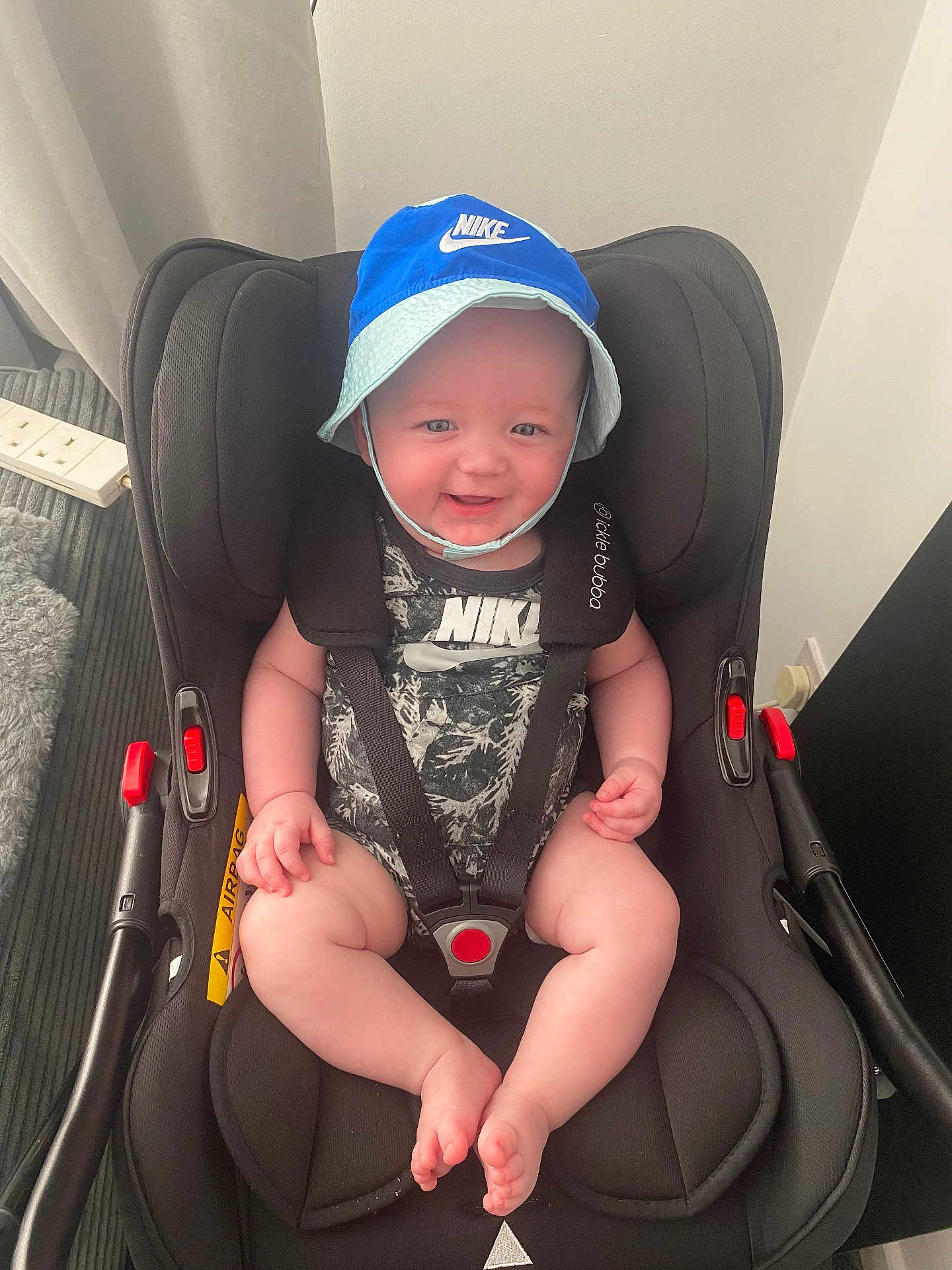 Arlo joined the competition — help win amazing prizes! baby, child, smiling, hat, nike, car_seat, straps, indoors, happy, seated, footwear_absent, clothing, infant, safety, smile, cute, headwear, face, person, young