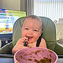Arlo is registered to the contest to win money with this photo: baby, high_chair, food, bowl, spoon, messy, happy, smiling, indoor, child, feeding, face, clothing, television, curtain, window, furniture, person, cute, infant