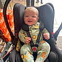 baby, car_seat, smiling, infant, onesie, animal_print, lion, tiger, straps, black_car_seat, store, shopping_cart, orange_bags, person, legs, shoes, door, floor_mat, happy, indoor