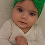 baby, child, green_bow, headband, white_outfit, arms_crossed, curious_expression, wide_eyes, infant, portrait, close_up, cute, indoor, person, skin, face, hands, young_child, headwear, soft_lighting