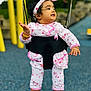 Nidhyanti is registered to the contest to win money with this photo: baby, child, swing, playground, outdoor, pink_clothing, headband, happy, smiling, childrens_play_area, footwear, bracelet, anklet, black_swing_seat, yellow_swing_frame, blue_floor, grass, trees, daylight, portrait