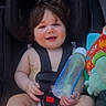 baby, infant, child, car_seat, portrait, smiling, happy, brown_hair, bottle, plush_toy, toy, seat_belt, harness, automobile, outdoor, sunlight, hand, sitting, baby_feet, colorful