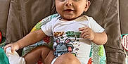 Baby Jose is registered to the contest to win money with this photo: baby, infant, child, onesie, play_mat, smiling, happy, cute, sock, floor, colorful, animal_design, indoor, toddler, clothing, diaper, person, young_child, cute_face, sitting
