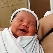 Baby Jose is registered to the contest to win money with this photo: newborn, baby, smiling, wrapped, blanket, hat, hospital, arm, tattoo, indoor, cabinet, door, person, infant, peaceful, sleeping, closeup, cute, human, portrait