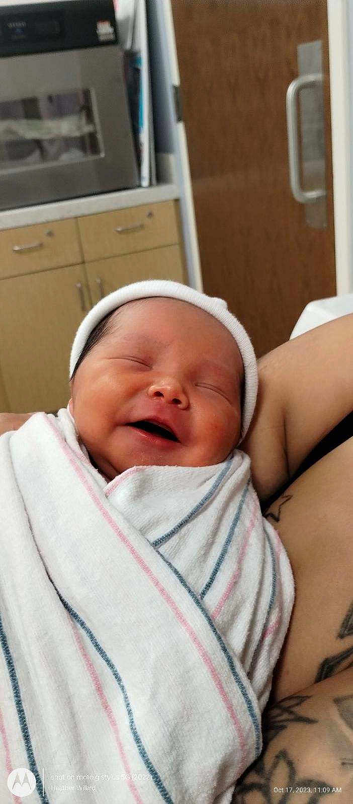 Baby Jose is registered to the contest to win money with this photo: newborn, baby, smiling, wrapped, blanket, hat, hospital, arm, tattoo, indoor, cabinet, door, person, infant, peaceful, sleeping, closeup, cute, human, portrait