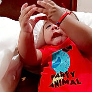 Antonio joined the competition — help win amazing prizes! baby, child, infant, red_clothing, onesie, hand, face, curious, lying_down, bed, bracelet, drool, skin, furniture, wood, white_bed_sheet, closeup, portrait, indoors, cute