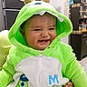 baby, child, costume, green, monster, smiling, indoor, kitchen, fridge, decoration, snowman, hood, cute, happy, apparel, person, screenshot, social_media, caption, home