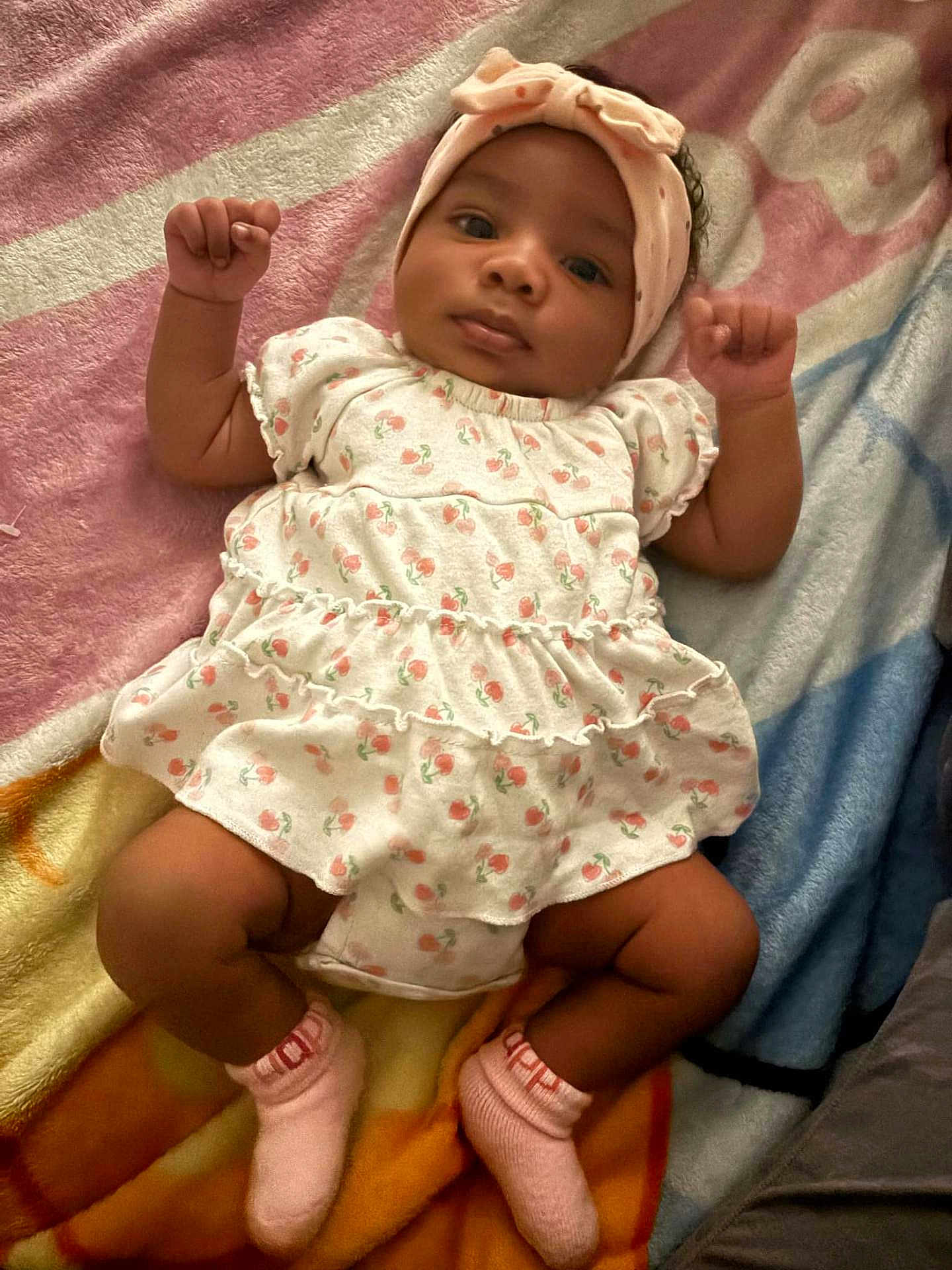 Leilani joined the competition — help win amazing prizes! baby, infant, child, blanket, headband, dress, patterned_clothing, socks, pink, cute, lying_down, fist, curious, soft_texture, indoor, portrait, young_child, cozy, colorful, calm