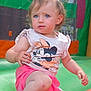 blue_eyes, bracelet, child, colorful, curly_hair, cute, earrings, face, green, inflatable, minnie_mouse, orange, outdoor, pink_shorts, playground, pony_tail, sitting, summer, toddler, tshirt