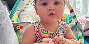 Sarah is registered to the contest to win money with this photo: baby, child, doll, curly_hair, sitting, indoor, couch, toy, colorful, cute, infant, clothing, patterned_dress, face, hands, curtains, window, soft_light, home, person
