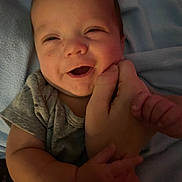 Ant is registered to the contest to win money with this photo: baby, smiling, hand, infant, person, clothing, skin, face, happy, cute, child, holding, fingers, closeup, portrait, young, expression, lying, blanket, soft