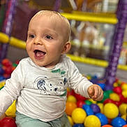 élio a rejoint le concours — aidez-le/la à gagner de superbes lots ! baby, child, smiling, happy, ball_pit, colorful, playground, toys, indoor, cute, infant, joyful, clothing, white_shirt, green_pants, face, portrait, play, fun, young