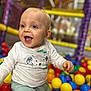 baby, child, smiling, happy, ball_pit, colorful, playground, toys, indoor, cute, infant, joyful, clothing, white_shirt, green_pants, face, portrait, play, fun, young