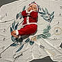 baby, child, santa_outfit, red_clothing, blanket, leaf_pattern, numbers, floor, cute, smiling, holiday, christmas, infant, lying_down, hands, feet, cozy, festive, decoration, portrait