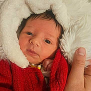 Caspian is registered to the contest to win money with this photo: baby, infant, face, red_sweater, white_hood, hand, person, portrait, cute, warm_clothing, knitwear, newborn, skin, eyes, expression, indoor, holding, soft_texture, closeup, headgear