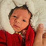 baby, infant, face, red_sweater, white_hood, hand, person, portrait, cute, warm_clothing, knitwear, newborn, skin, eyes, expression, indoor, holding, soft_texture, closeup, headgear