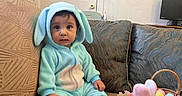 Alen joined the competition — help win amazing prizes! baby, child, bunny_costume, onesie, sitting, couch, plush_toy, rabbit, easter_eggs, pastel_colors, flowers, basket, living_room, indoor, portrait, wide_eyed, infant, cushions, television, balloon