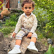 Alen joined the competition — help win amazing prizes! child, toddler, portrait, sitting, outdoors, garden, tree, tree_trunk, greenery, plants, leaves, clothing, shirt, suspenders, plaid_pants, sneakers, socks, direct_gaze, natural_light, garden_pots