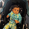Alen is registered to the contest to win money with this photo: baby, child, infant, stroller, portrait, sitting, indoors, home, plaid, overalls, colorful_clothing, star_pattern, wide_eyed, looking_at_camera, brown_hair, cozy, houseplant, curtains, furniture, photography