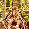child, toddler, royal, crown, costume, prince, portrait, outdoor, garden, fountain, ornate, velvet, embroidery, gold, jewels, seated, smiling, formalwear, palace, flowers