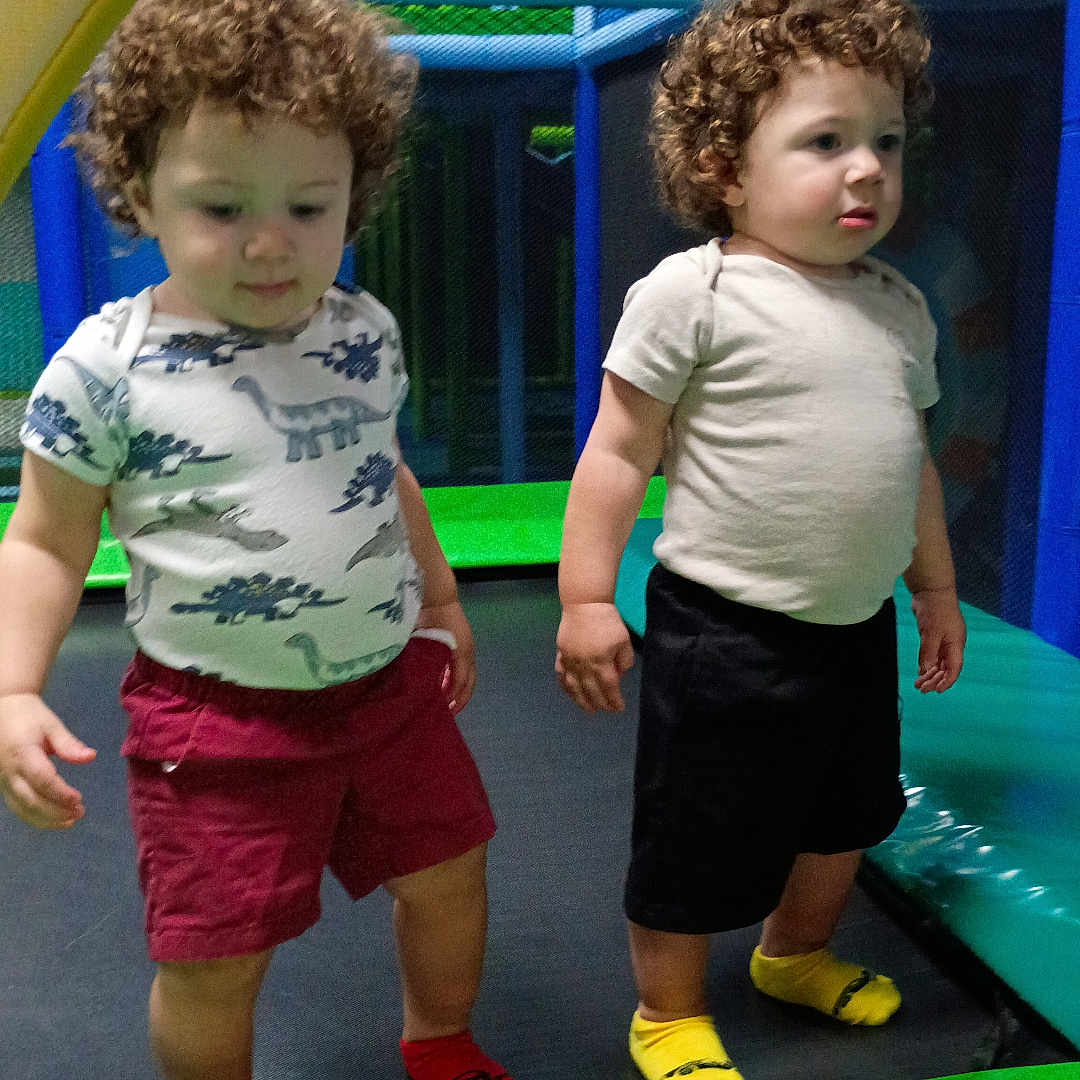 Azure is registered to the contest to win money with this photo: child, toddler, curly_hair, indoor_play_area, playground, dinosaur_shirt, shorts, socks, colorful, netting, play_equipment, standing, two_children, fun, kids, play, smile, casual_clothing, young_children, active