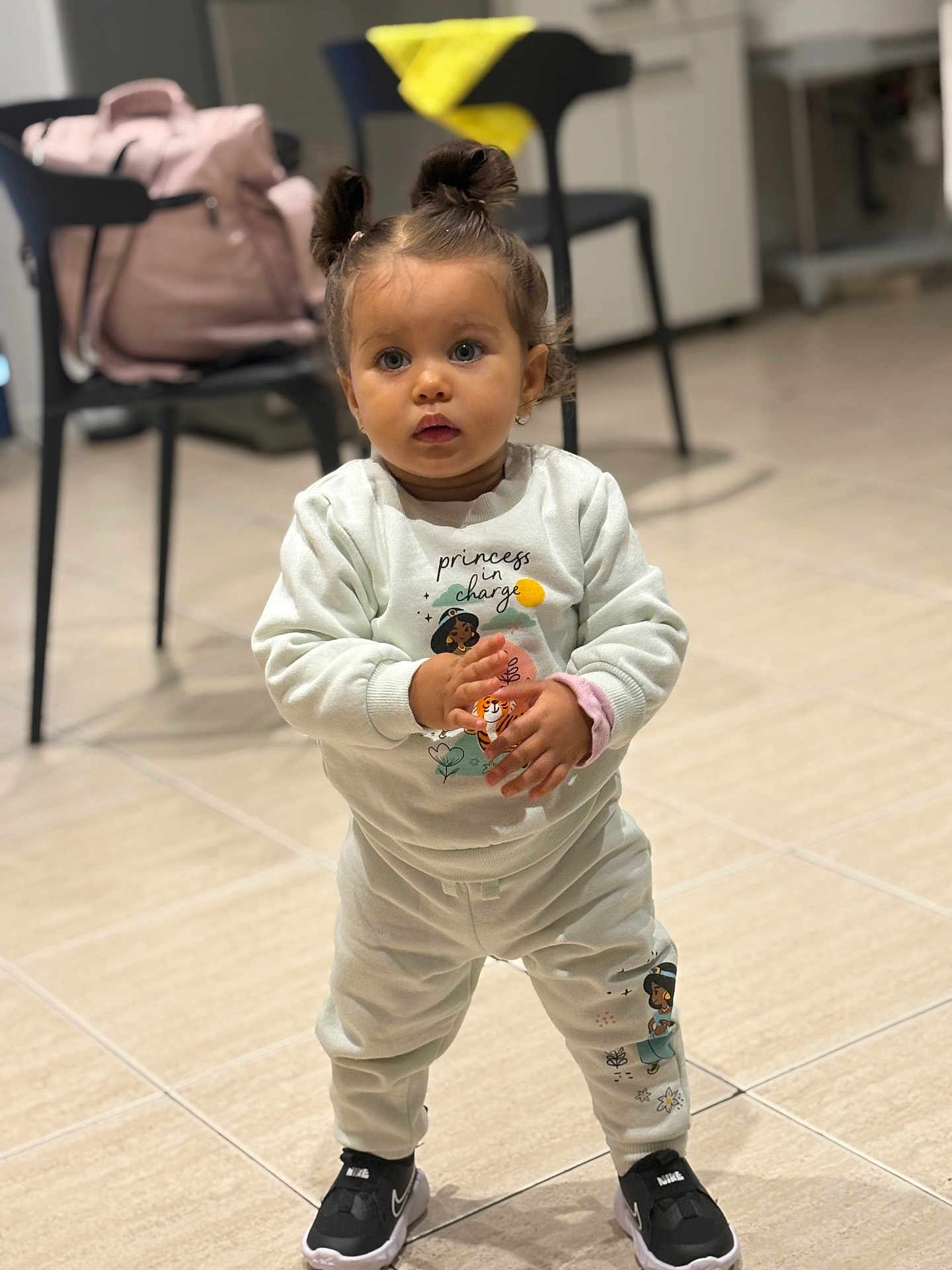 Syana a rejoint le concours — aidez-le/la à gagner de superbes lots ! toddler, child, standing, indoor, clothing, sweatshirt, pants, nike, shoes, hair_buns, face, eyes, floor, tile, bag, chair, background, person, cute, portrait