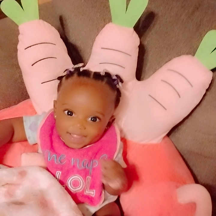 Avaeha joined the competition — help win amazing prizes! baby, bib, blanket, braids, carrot_pillow, child, clothing, couch, cozy, cute, happy, home, indoors, infant, person, pillow, portrait, seated, smiling, soft_toy