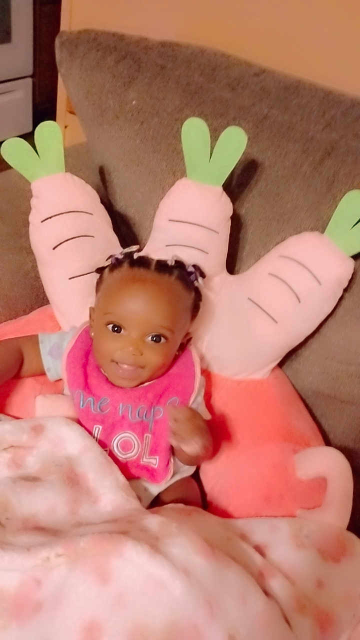 Avaeha joined the competition — help win amazing prizes! baby, child, smiling, braids, bib, blanket, couch, pillow, carrot_pillow, indoors, cute, happy, seated, infant, clothing, home, soft_toy, person, portrait, cozy