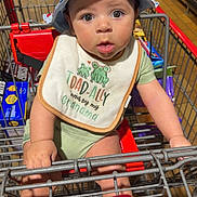 Princeton joined the competition — help win amazing prizes! baby, shopping_cart, hat, bib, grocery_store, child, infant, curious, retail, aisle, floor, green_clothing, red, metal_cart, drool, seat, person, cute, wide_eyes, shopping