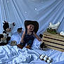 baby, cowboy_hat, denim_overalls, plush_cow, chicks, wooden_crate, ceramic_hen, eggs, blanket, smiling, sitting, cute, indoors, decor, child, toy, animal, farm_theme, portrait, happy