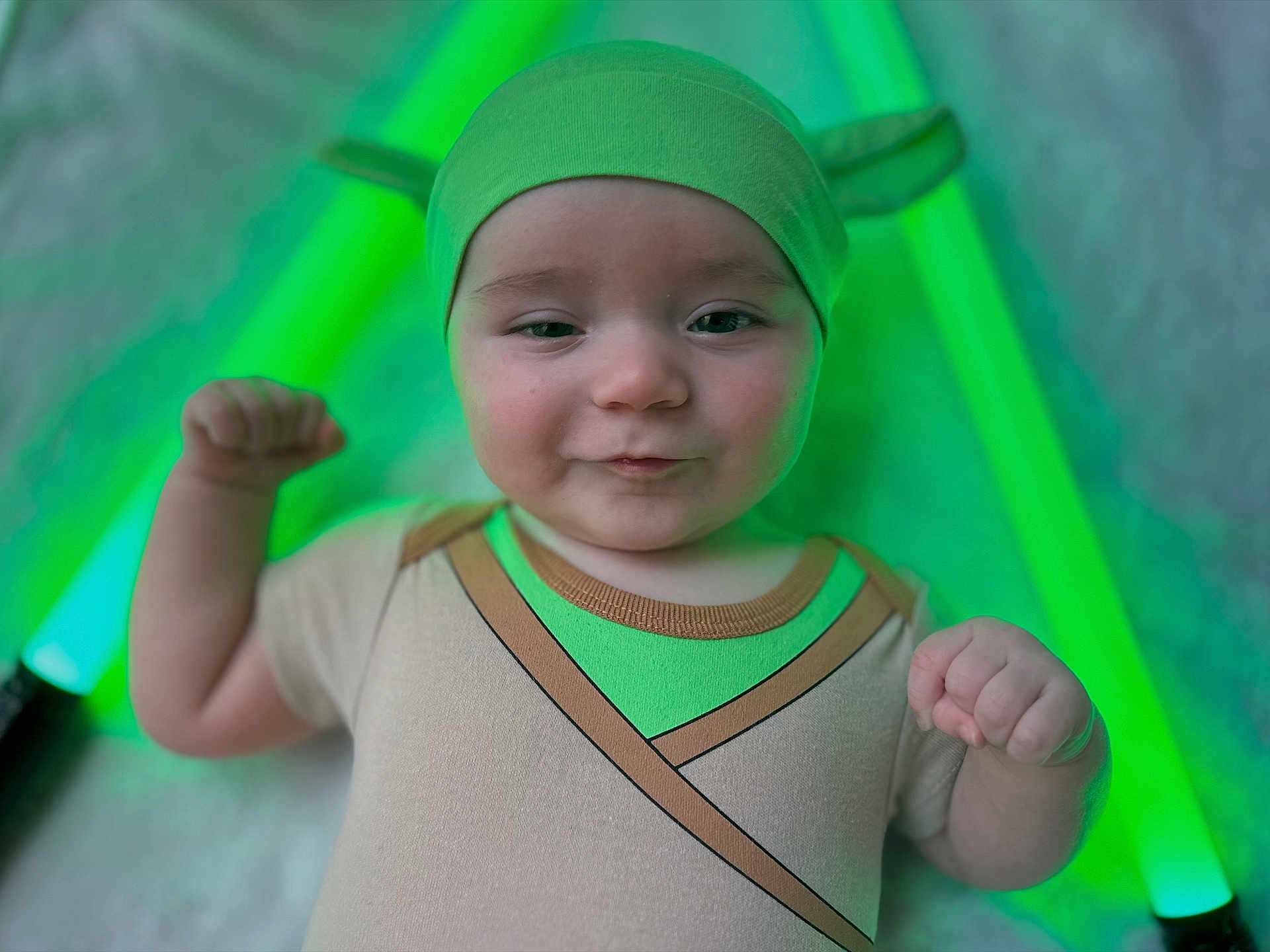 Mason is registered to the contest to win money with this photo: baby, child, costume, green, lightsaber, star_wars, headwear, infant, cute, portrait, flexing, toy, playful, closeup, indoor, smiling, face, person, fun, green_light
