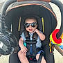 baby, child, car_seat, sunglasses, toy, fan, outdoor, seatbelt, cute, tongue_out, infant, summer, shade, baby_clothes, colorful, plastic_toy, stroller_accessory, happy, person, small_child