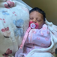 Ariyah is registered to the contest to win money with this photo: baby, blanket, pacifier, infant, sleeping, pink_clothing, floral_pattern, soft_texture, cozy, cute, child, indoor, newborn, wrapped, face, head, person, resting, comfort, toddler