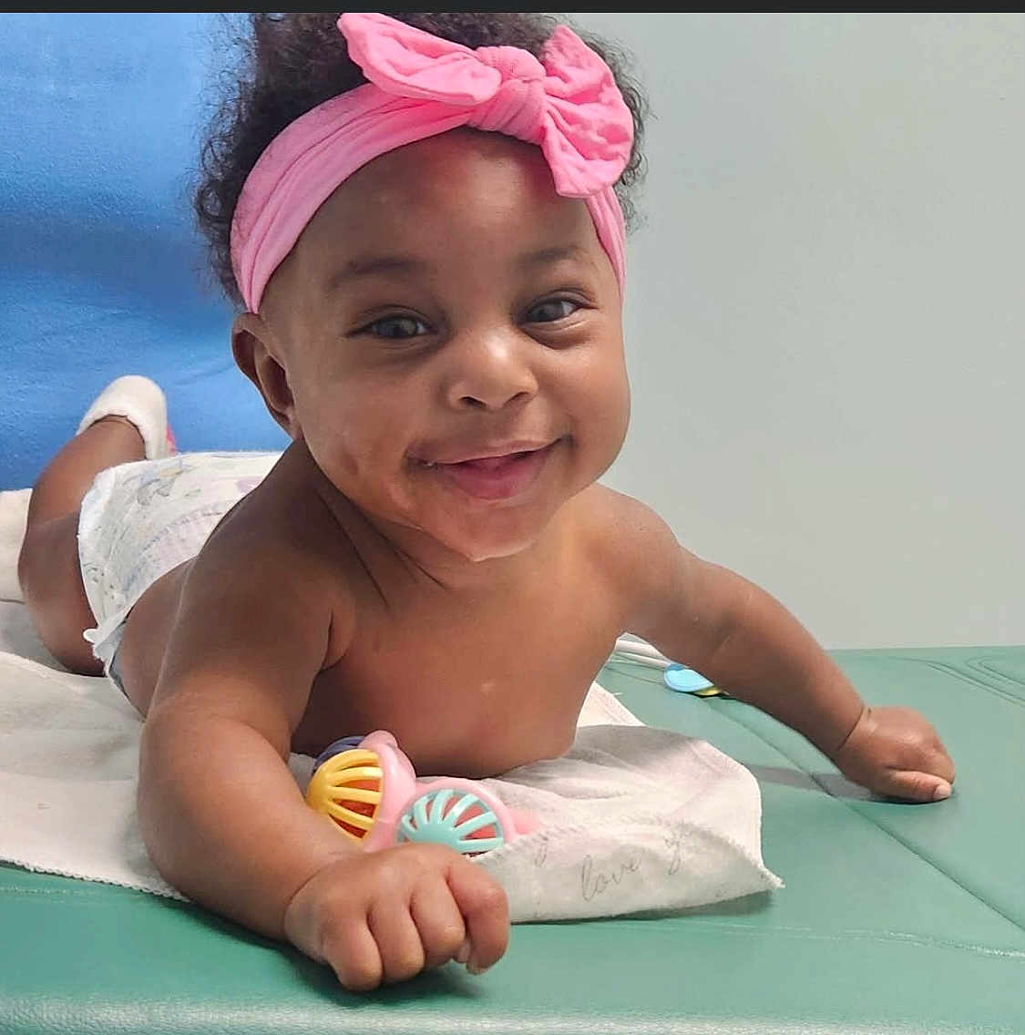 Ariyah is registered to the contest to win money with this photo: baby, infant, smile, headband, pink, bow, toy, diaper, tummy_time, cute, child, happy, indoor, skin, hand, face, expression, play, young, lying_down