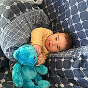 Lúca participe au concours pour gagner de l'argent avec cette photo : baby, blanket, blue, child, comfort, cozy, cuddly, cute, gray, indoors, pattern, person, plush_toy, portrait, resting, smiling, soft, teddy_bear, warm, young