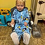 Abel is registered to the contest to win money with this photo: toddler, child, pajamas, blue, smiling, sitting, chair, toy, floor, plastic_jug, indoor, playful, happy, person, face, feet, carpet, cabinet, yellow_wall, home