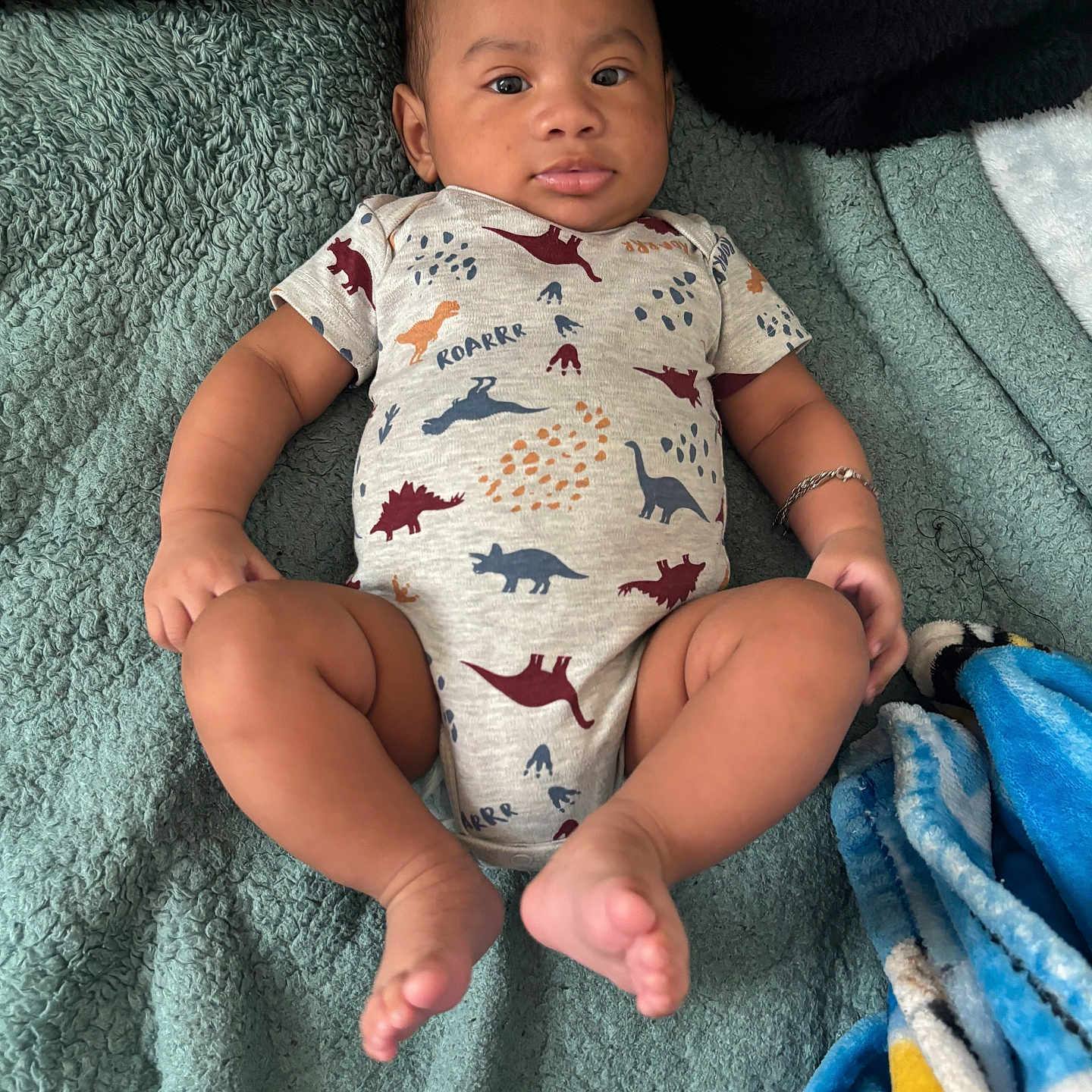 Kontrevius Robinson joined the competition — help win amazing prizes! baby, infant, child, onesie, dinosaur_pattern, bracelet, blanket, blue_blanket, yellow_blanket, lying_down, curious, skin, arm, leg, foot, face, expression, indoors, cozy, soft