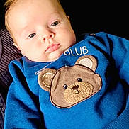 Diago León joined the competition — help win amazing prizes! baby, child, infant, blue_sweater, teddy_bear_patch, face, eyes, hand, clothing, couch, indoors, person, cute, portrait, skin, young, warm, relaxed, soft_light, cozy