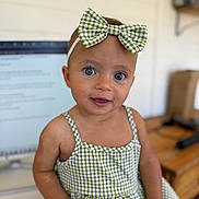 Etta is registered to the contest to win money with this photo: baby, child, girl, blue_eyes, bow, headband, green_checkered, dress, sitting, indoor, computer_screen, blurred_background, face, smile, person, cute, portrait, infant, skin, hand