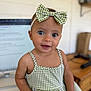 baby, child, girl, blue_eyes, bow, headband, green_checkered, dress, sitting, indoor, computer_screen, blurred_background, face, smile, person, cute, portrait, infant, skin, hand