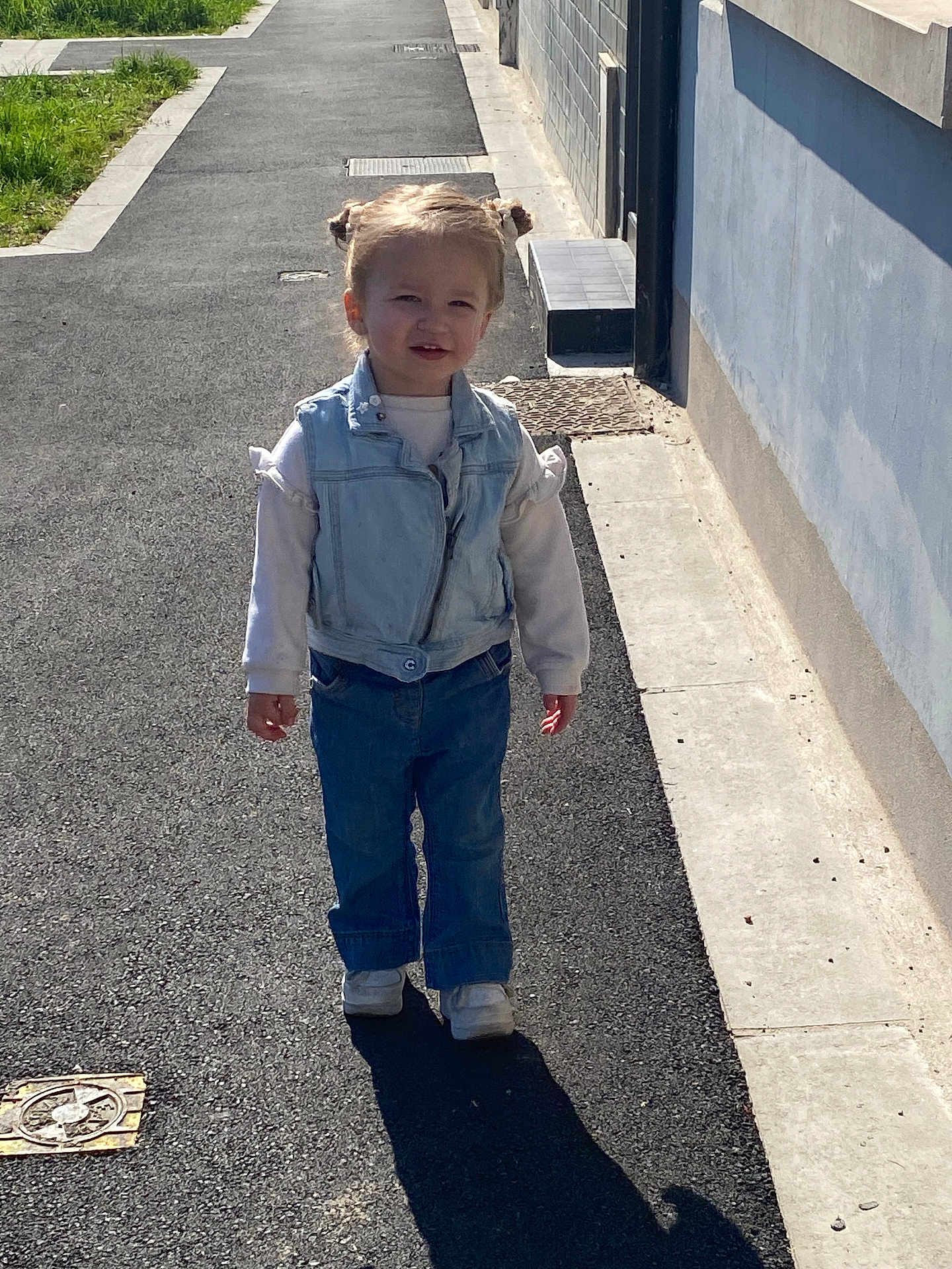 Lyahna a rejoint le concours — aidez-le/la à gagner de superbes lots ! child, toddler, denim_vest, jeans, white_sneakers, outdoor, sidewalk, sunny, shadow, hair_buns, walking, casual_clothing, smiling, pavement, daylight, urban, person, small_child, cute, happy