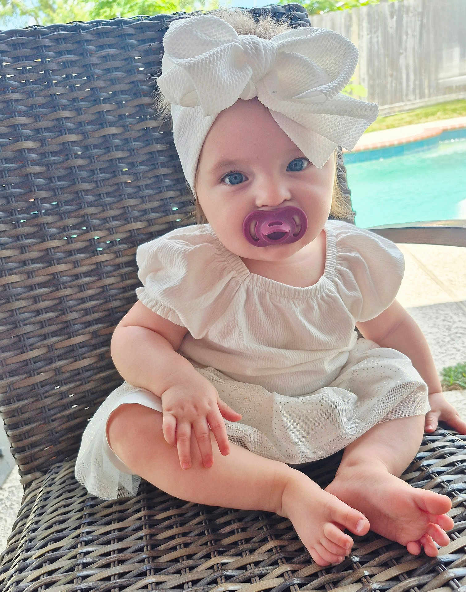 Evelynn is registered to the contest to win money with this photo: baby, child, pacifier, headband, bow, dress, white_clothing, blue_eyes, wicker_chair, outdoor, pool, garden, summer, sitting, cute, infant, portrait, daylight, relaxing, happy