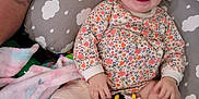 Evelynn is registered to the contest to win money with this photo: baby, child, smile, toy, cow_toy, pillow, cloud_pattern, floral_clothing, tattoo, arm, blanket, happy, infant, cute, indoor, person, playful, lying_down, colorful, relaxed