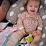 baby, child, smile, toy, cow_toy, pillow, cloud_pattern, floral_clothing, tattoo, arm, blanket, happy, infant, cute, indoor, person, playful, lying_down, colorful, relaxed