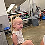Ella joined the competition — help win amazing prizes! child, girl, blonde_hair, black_bow, white_top, shorts, sitting, blue_bench, indoor, cafeteria, food_court, drink_display, people, floor, table, trash_can, casual_clothing, curious, portrait, candid
